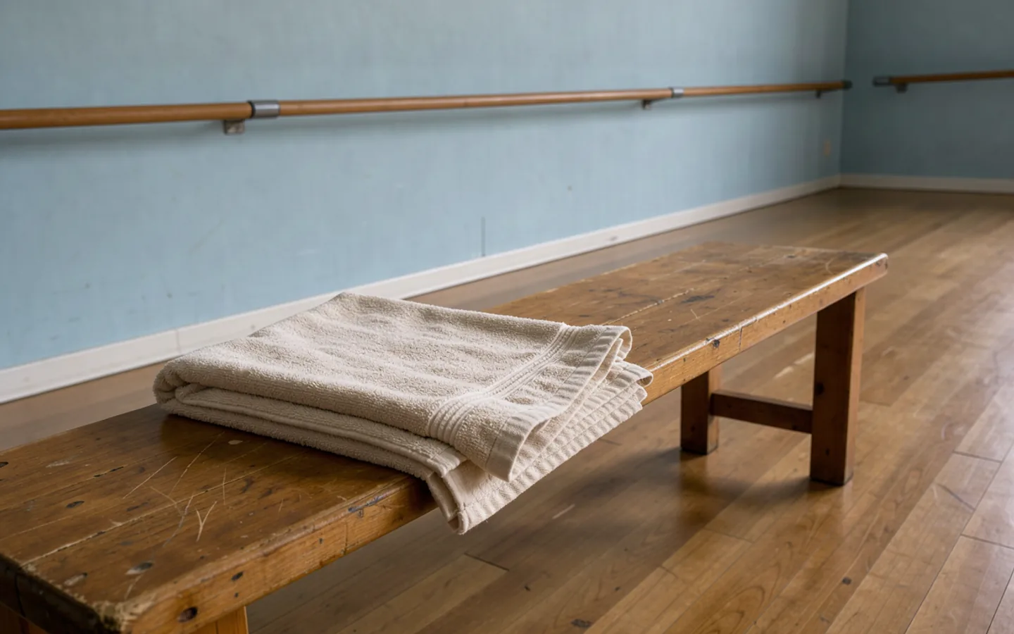 A plain cotton towel rests on a wooden bench in a quiet rehearsal room.